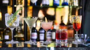 Fünf stilvolle Cocktails in verschiedenen Gläsern an einer Bar.