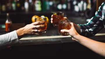 Drei Hände stoßen mit Getränken in einer Bar an.