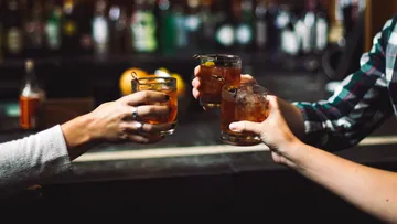 Three hands toast drinks in a bar.