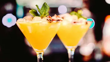 Zwei Cocktails mit Eiswürfeln und Minze auf einem Tisch.