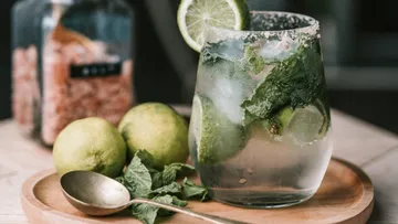 Glas mit Mojito, mit Limetten und Minze, auf Holztablett.