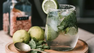 Glass with mojito, fresh lime and mint on a tray.