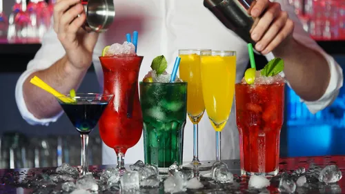 Colourful cocktails are prepared and served at a bar.