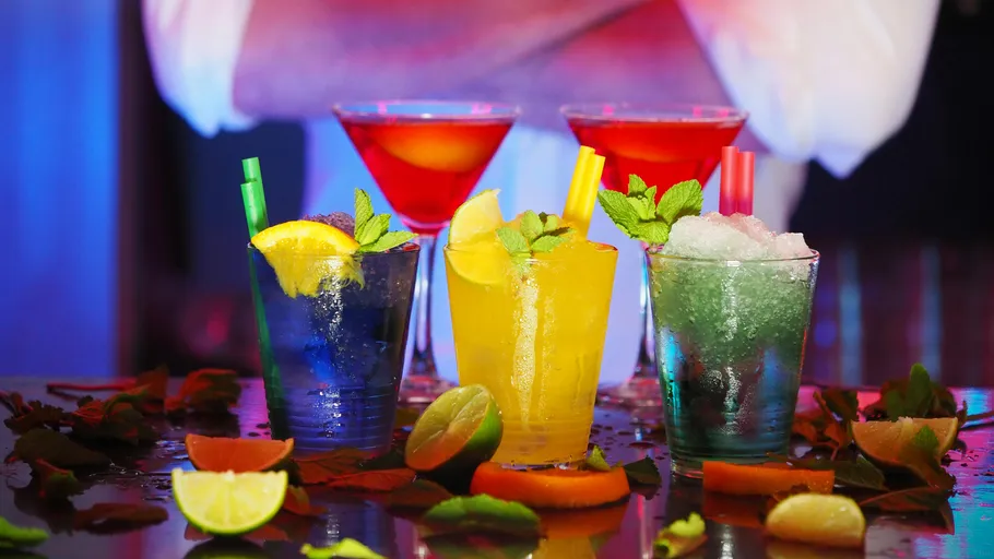 Colourful cocktails sit on a table surrounded by fresh fruit.