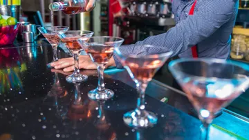 A bartender pours cocktails into glasses at the bar.