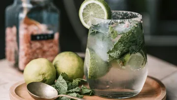 Ein Glas Mojito mit Limetten und Minze auf Tablett.