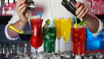 Barkeeper schüttelt Cocktails vor bunten Gläsern in Bar.