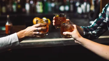 Three hands hold cocktails at a bar.