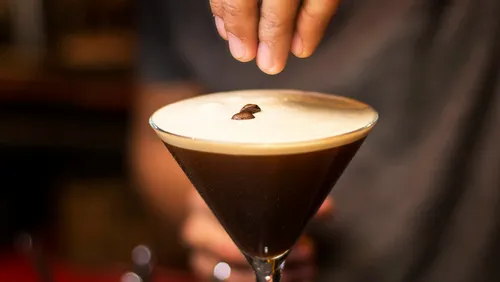 Cocktail with foam is decorated with coffee bean.