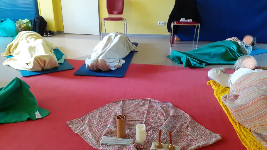 People lie on mats surrounded by blankets and objects.