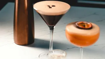 Zwei Cocktails stehen neben einer Metallflasche auf einem Tisch.