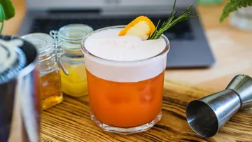 Ein Cocktail steht auf einem Holztisch neben Zubehör.