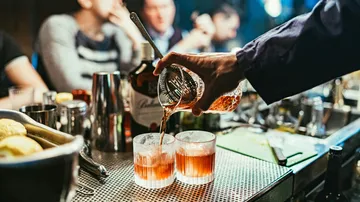 A bartender pours cocktails into two glasses.