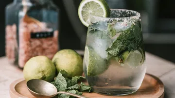 Ein Glas Mojito steht auf einem Holzbrett.