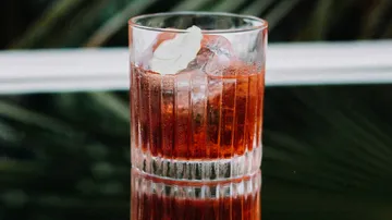 Glas mit Eis und rotem Getränk auf schwarzem Tisch.