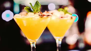 Zwei Cocktails mit Eis, Früchten und Minze, beleuchtet.