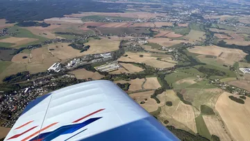 Flugzeugflügel über landwirtschaftlichen Feldern und kleinen Städten.