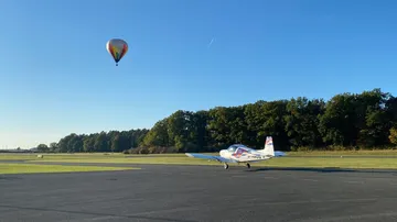 Heißluftballon schwebt über einem aufrollenden Flugzeug auf dem Platz.