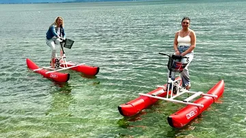 Two women ride on red water bikes in the lake.