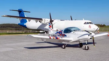 Two airplanes are parked on an asphalt parking lot under clear skies.