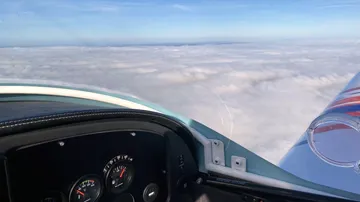 Cockpit instruments show a blue sky above the clouds.