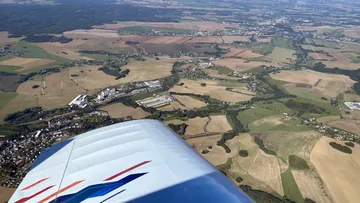 Flügel eines Flugzeugs schwebt über grüne Felder und Dörfer.