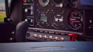 Cockpit with steering wheel and aircraft logbook on instrument panel.