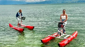 Zwei Frauen fahren auf roten Wasserfahrrädern im See.