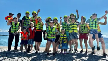 Group of cheerful kids in life jackets jumping at the water.