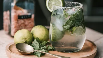 Glas mit Mojito, umgeben von Limetten und Minze.
