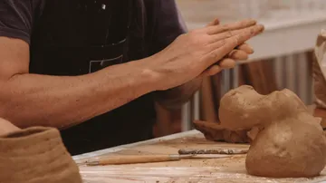 Hands form clay objects on a table in a studio.