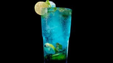 Blue cocktail with lime and mint on black background.