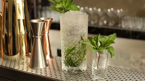 Ein Glas Mojito steht auf einer Bartheke mit Minze.