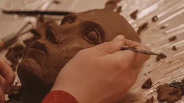 Hände modellieren eine Tonskulptur auf einem Tisch.