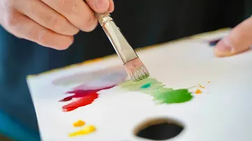 Pinsel mischt Farben auf einer Palette. Hintergrund ist unscharf.