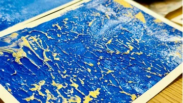Blauer Hintergrund mit goldenen, wirbelnden Farbmusterungen.