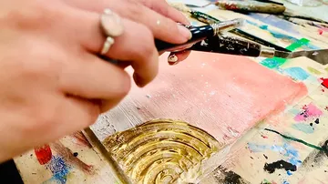 Hand mit Pinsel malt goldenen Bogen auf Farbhintergrund.