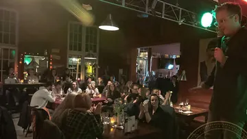 Ein Komiker spricht, während das Publikum applaudiert in einem Lokal.