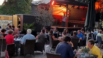 Tische mit Gästen, die ein Konzert im Freien genießen.
