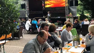 Menschen sitzen bei Tisch, während eine Aufführung auf der Bühne stattfindet.