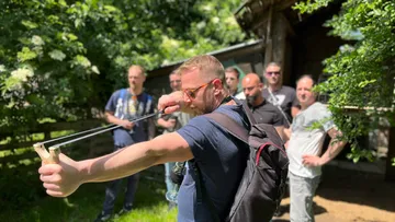 Mann zielt mit einer Schleuder auf ein Ziel, umgeben von Zuschauern.