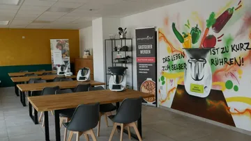 Küchenraum mit Tischen, Küchengeräten und buntem Wandbild.