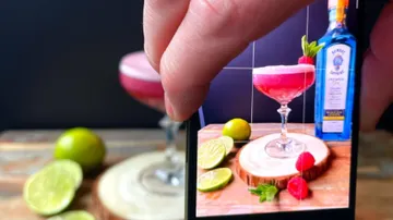 Cocktailglas wird fotografiert, umgeben von Limetten und Holz.
