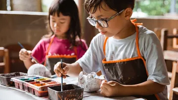 Children paint clay pots in a room full of light.