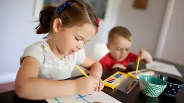 Kinder malen konzentriert mit Buntstiften am Tisch.