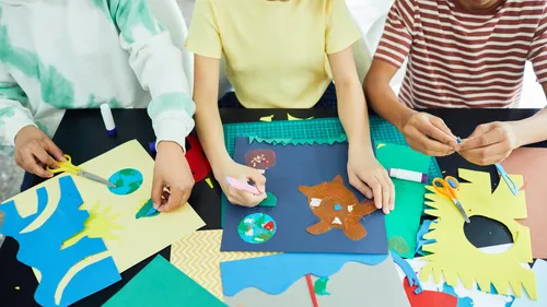 Three people are making crafts with colorful paper and materials.
