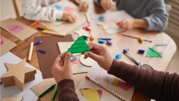 Colourful craft materials on a table, someone holding a green piece.