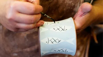 Tasse bemalt mit Fischmotiven von Hand. Atelierumgebung.