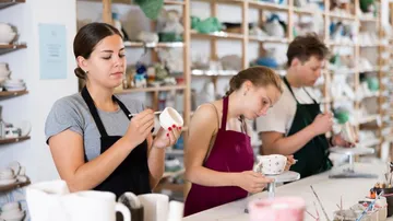Drei Personen bemalen Töpferwaren in einem Atelier.