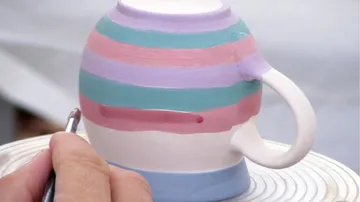 Eine Tasse wird mit bunten Streifen bemalt.